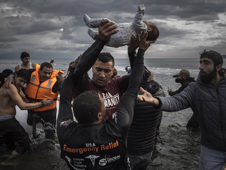 Un voluntario sostiene a un bebé mientras otros tratan de ayudar a un grupo de refugiados 
que acaba de alcanzar las costas de la isla griega de Lesbos tras permanecer varias horas en el mar a la deriva, miércoles 25 de noviembre, 2015.